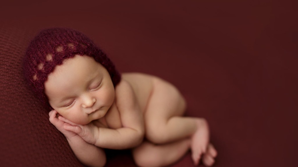 Sweet baby girl on her side, this is a table pose or beanbag pose. This is not considered a wrapped pose. Baby on burgandy fabric with a matching bonnet. Taken in-studio by Shelly Rosen Photograpy in San Diego, Ca. San Diego newborn photographer.