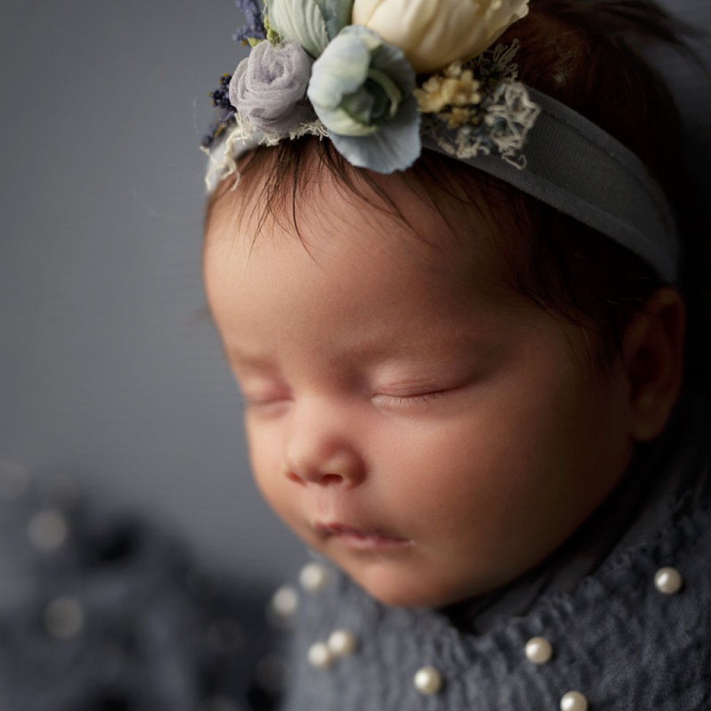 Baby girl in profile on blue fabric backdrop with a pretty pearl layer. Taken in San Marcos, Ca by Shelly Rosen Potography in her portrait studio.