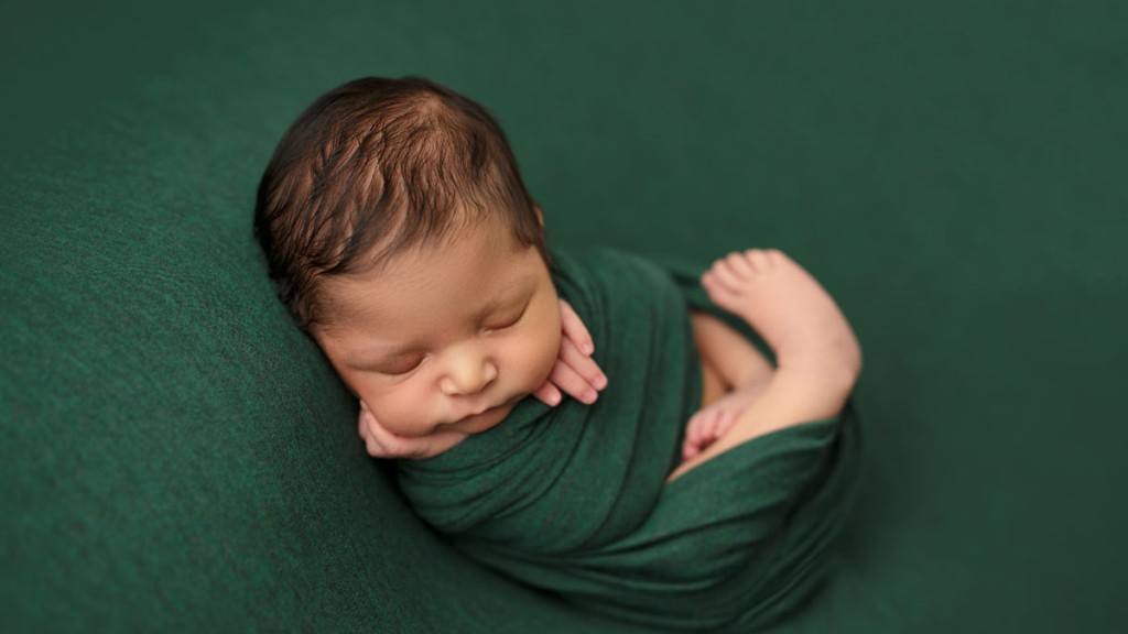 Baby wrapped in a green wrap and posed on a table or beanbag. This wrapped pose is a favorite of Shelly Rosen, San Marcos newborn photography is her passion.