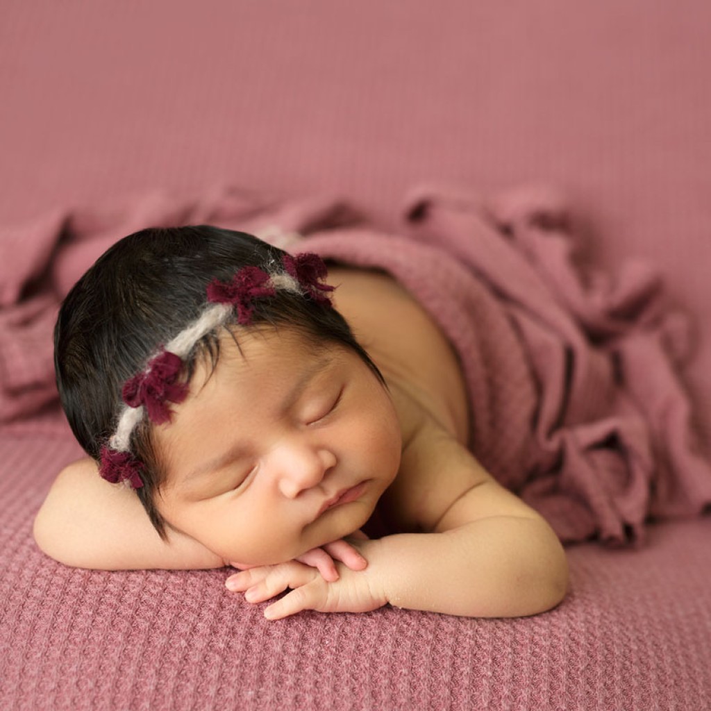 Beautiful baby girl on a mauve fabric backdrop. This is considered a table pose, a beanbag pose or a semi-nude pose. This is not a wrapped pose, as baby is not wrapped.