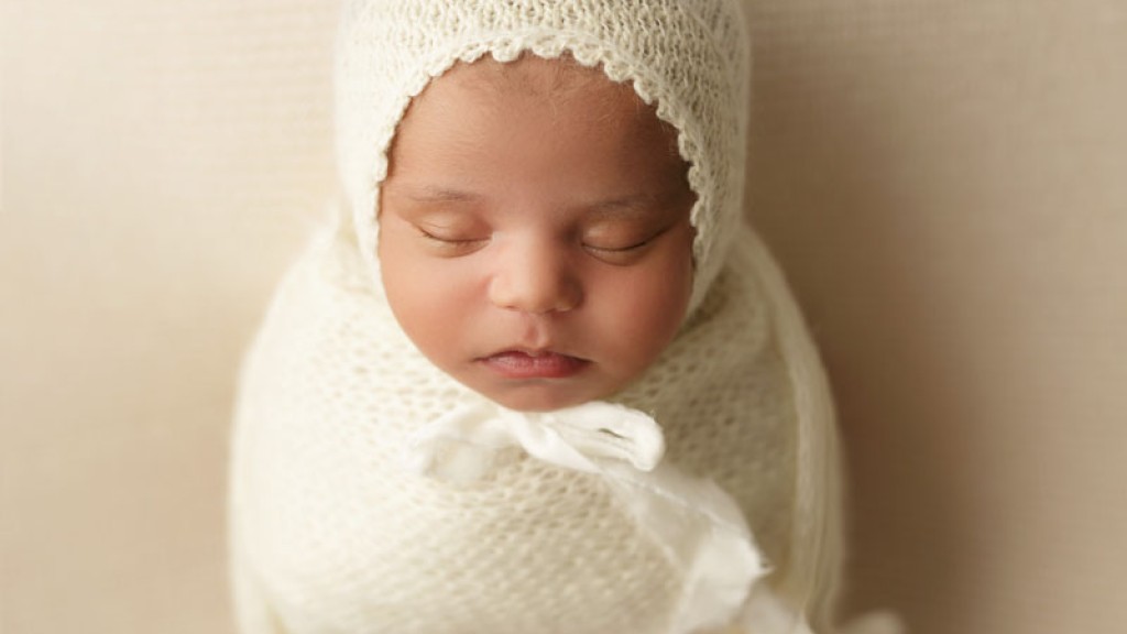 Oceanside newborn photographer and Vista newborn photography shows this wrapped-up baby girl in a swaddled pose on cream fabric. Her little legs are stickin gout of her wrap so you can see her sweet legs and feet.