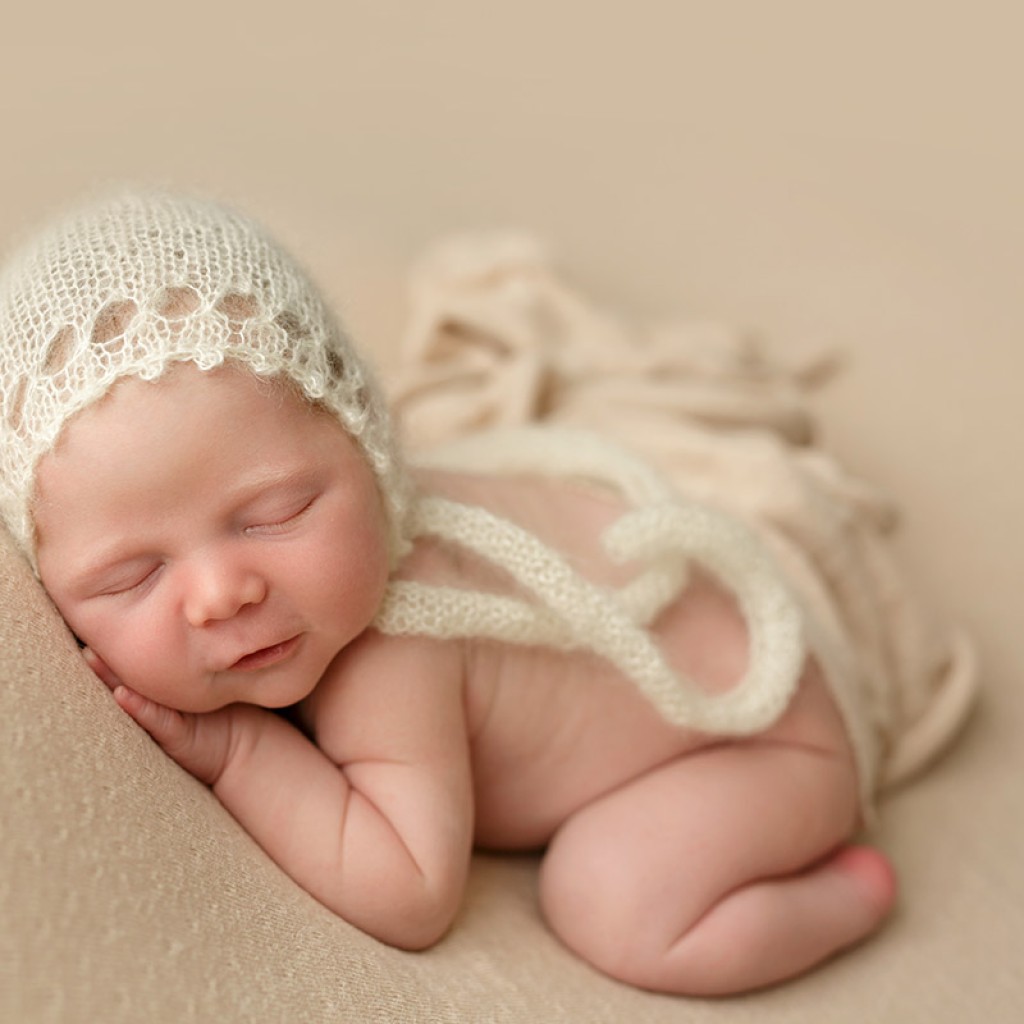 This table pose is of a pretty baby girl usung a cream colored fabric and cream bonnet.