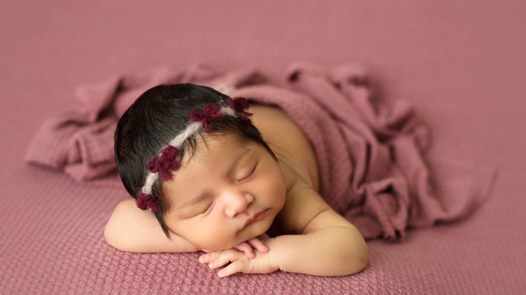 sweet baby girl on mauve fabric backdrop with a headband full of little bows.